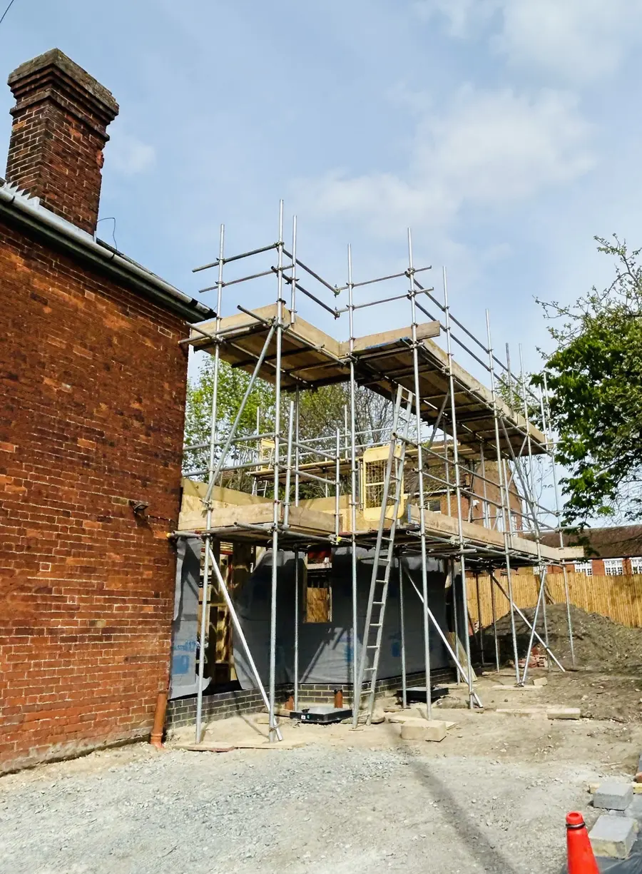 Scaffold around a new timber-frame structure beside a brick house